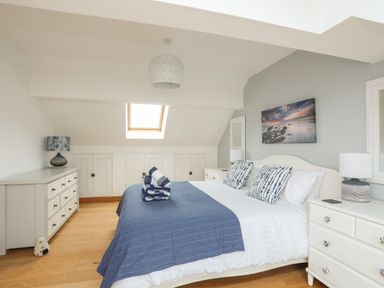 A bedroom with a bed covered in blue and white linens and pillows with dressers and lamps at Red Ridge in Llandanwg near Harlech