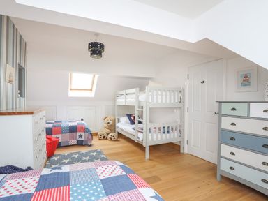 A children's bedroom with bunk beds a single bed dressers and wooden flooring at Red Ridge in Llandanwg near Harlech