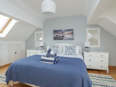 A bedroom with a double bed with blue bedspread two bedside tables with lamps two mirrors and a skylight window at Red Ridge in Llandanwg near Harlech