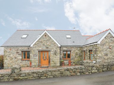 A stone house with wooden doors and windows and a slate roof behind a low stone wall at Red Ridge in Llandanwg near Harlech