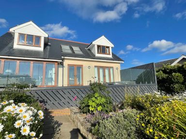 A two story house with dormer windows and glass doors with a garden and flowers in front at Red Ridge in Llandanwg near Harlech