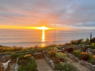 A stone garden with plants and seating overlooking the ocean at sunset at Red Ridge in Llandanwg near Harlech