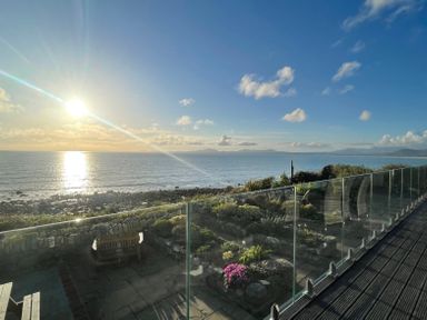 A patio with wooden benches and garden area overlooking the ocean with a glass railing at Red Ridge in Llandanwg near Harlech