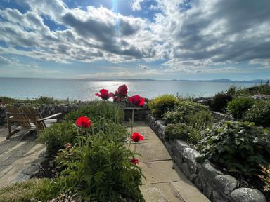 A garden with red flowers and wooden chairs overlooking the sea at Red Ridge in Llandanwg near Harlech