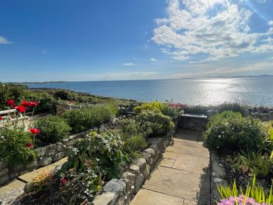 A stone-paved garden pathway with plants and flowers overlooking the sea at Red Ridge in Llandanwg near Harlech