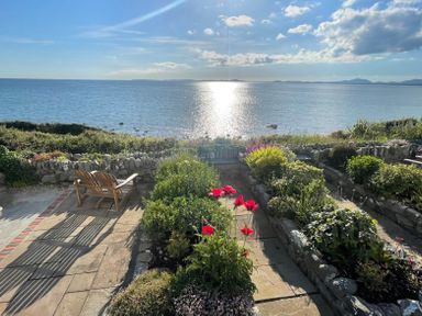 A garden with flowering plants and a wooden bench overlooking the sea at Red Ridge in Llandanwg near Harlech