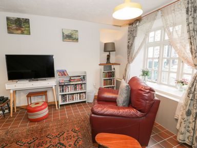 A sitting room with a red leather chair television and bookshelf near a window at 3 Alma Terrace in Llanfairfechan