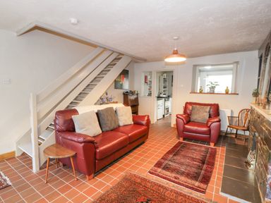 A living room with red leather sofa and armchair with cushions and a small wooden side table at 3 Alma Terrace in Llanfairfechan