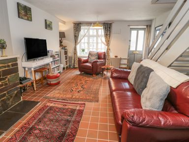 A living room with red leather sofa and armchair two patterned rugs and a television at 3 Alma Terrace in Llanfairfechan