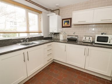 A kitchen with white cabinets a countertop sink toaster microwave and a framed picture on the wall at 3 Alma Terrace in Llanfairfechan
