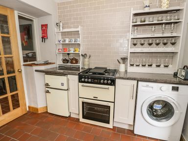 A kitchen with a refrigerator stove washing machine shelves with cups and glasses at 3 Alma Terrace Llanfairfechan