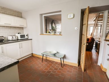 A kitchen with white cabinets toaster and microwave a bench with a bowl and a clock on the wall at 3 Alma Terrace in Llanfairfechan