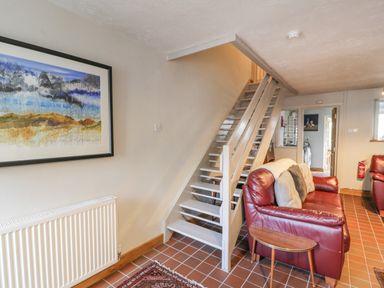 A living room with a red leather sofa, staircase, framed artwork on the wall, and a small table at 3 Alma Terrace in Llanfairfechan