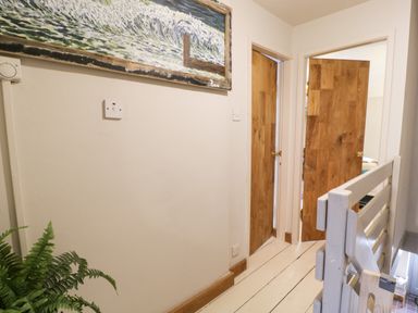 A hallway with wooden doors a painting on the wall a plant and white railing at 3 Alma Terrace in Llanfairfechan
