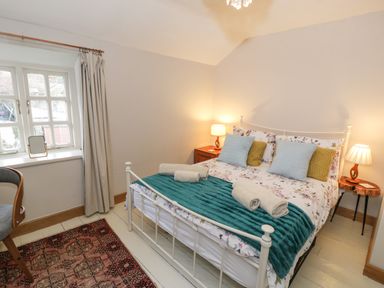 A bedroom with a double bed with cushions and bath towels a chair near the window and two bedside tables with lamps at 3 Alma Terrace in Llanfairfechan