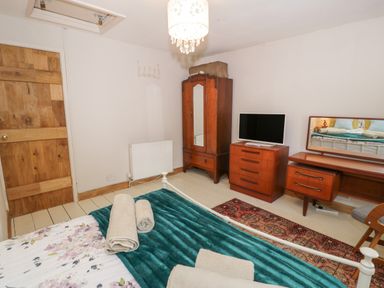 A bedroom with a bed, wooden wardrobe, dresser with a TV, and a vanity with a mirror at 3 Alma Terrace in Llanfairfechan