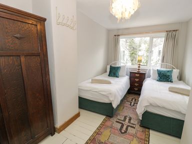 A bedroom with two single beds a wooden wardrobe a bedside table with a lamp and a patterned rug on the floor at 3 Alma Terrace in Llanfairfechan