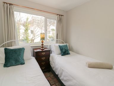 A bedroom with two single beds a bedside table with a lamp and a window with curtains at 3 Alma Terrace in Llanfairfechan