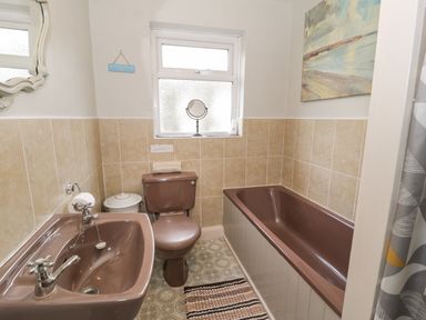 A bathroom with a pink sink toilet and bathtub tiled walls and a window at 3 Alma Terrace in Llanfairfechan