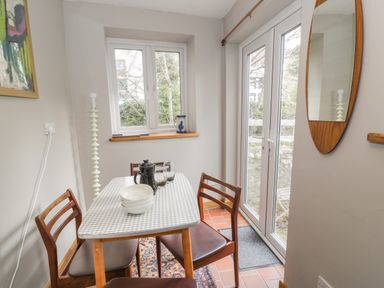 A dining area with a checkered tablecloth on a table set with bowls and glasses four wooden chairs a window a door leading outside and a tall lamp at 3 Alma Terrace in Llanfairfechan