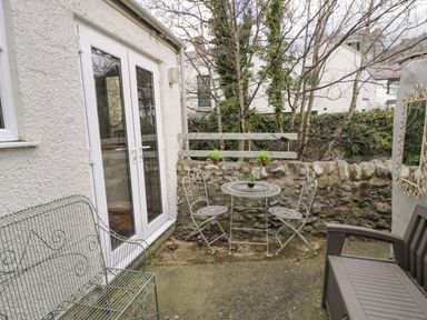 A small outdoor patio with metal chairs and table near a stone wall at 3 Alma Terrace in Llanfairfechan