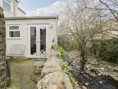 A patio with metal chairs and a table next to a small stream at 3 Alma Terrace in Llanfairfechan