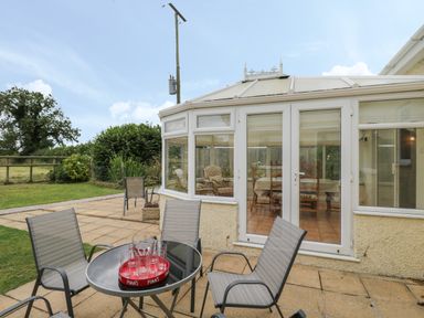 A patio with four chairs and a glass table with glasses in a tray outside a conservatory at Downs View in Norton Ferris