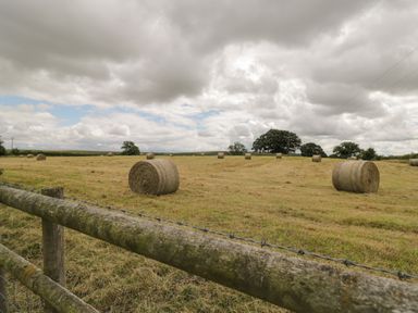 A field with round hay bales and a wooden fence under a cloudy sky at Downs View in Norton Ferris