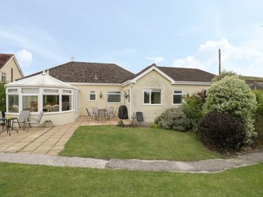 The back of a single story house with a patio and garden area with bushes at Downs View in Norton Ferris