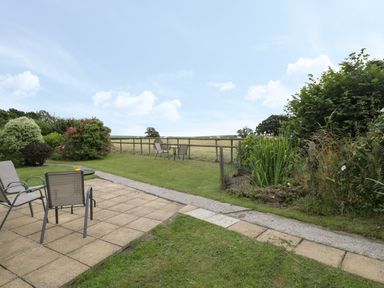 An outdoor garden area with patio furniture on a tiled area and a grassy section with a wooden fence and bushes at Downs View in Norton Ferris