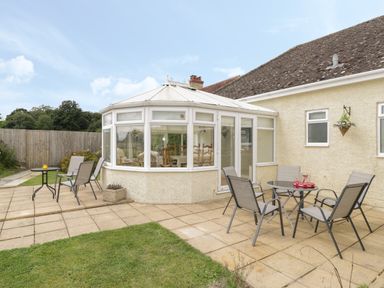 A patio area with outdoor tables and chairs next to a conservatory and garden at Downs View in Norton Ferris