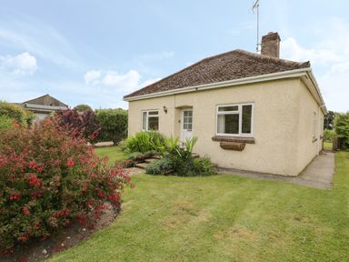A beige single-story house with a sloped roof surrounded by a lawn and bushes at Downs View in Norton Ferris