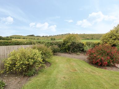 A garden with grass and bushes with a wooden fence and fields in the background at Downs View in Norton Ferris