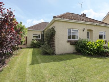 A yard with grass and plants around a beige house with windows at Downs View in Norton Ferris