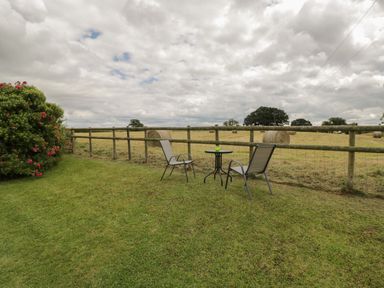 An outdoor area with two chairs and a small round table on grass near a wooden fence and hay bales in a field at Downs View in Norton Ferris