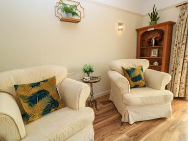 A sitting area with two cream armchairs and patterned cushions a wooden shelf and a small side table with flowers at Downs View in Norton Ferris