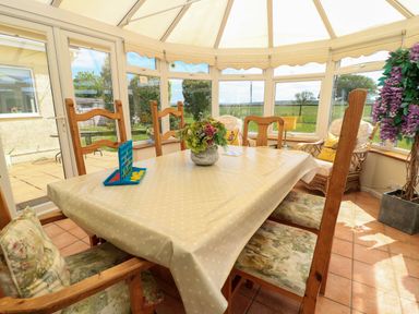 A conservatory dining area with a table covered in a polka dot tablecloth surrounded by wooden chairs and a board game at Downs View in Norton Ferris