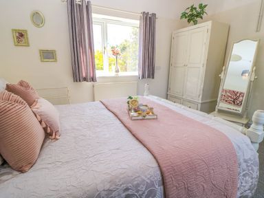 A bedroom with a bed covered in white and pink bedding a wooden wardrobe and a mirror at Downs View in Norton Ferris
