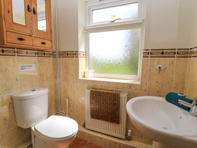 A bathroom with a toilet, sink, window, wooden cabinet, and radiator at Downs View in Norton Ferris