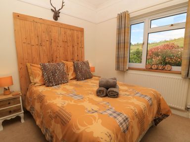 A bedroom with a wooden headboard orange patterned bedspread and folded towels on bed at Downs View in Norton Ferris