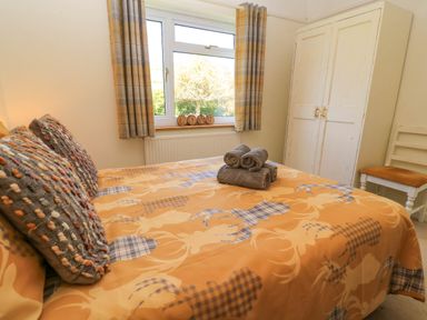 A bedroom with a bed covered in patterned bedding two pillows three towels on the bed a window with plaid curtains a white wardrobe and a chair at Downs View in Norton Ferris