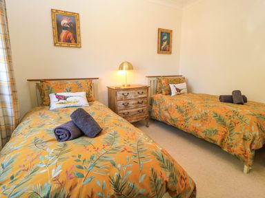 A bedroom with two single beds with leaf patterned bedding and a wooden nightstand with a lamp at Downs View in Norton Ferris