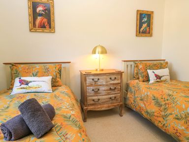 A bedroom with two single beds with orange bedding and a wooden dresser with a lamp at Downs View in Norton Ferris