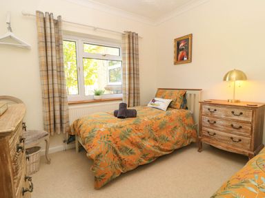 A bedroom with a single bed with orange patterned bedding next to a window with plaid curtains a wooden chest of drawers with a lamp and a framed picture on the wall at Downs View in Norton Ferris