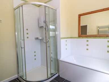 A bathroom with a corner shower cubicle and a bathtub with a wooden framed mirror at Downs View in Norton Ferris