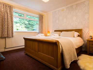 A bedroom with a wooden bed frame bedside tables and patterned curtains at Nutwood in Lakeside