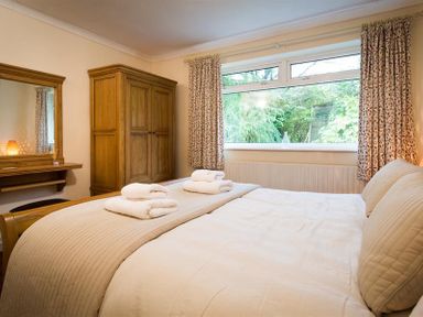 A bedroom with a large bed folded towels wooden wardrobe and dressing table with mirror at Nutwood in Lakeside