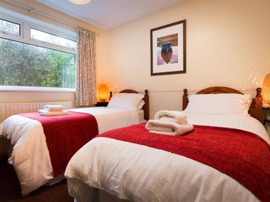 A bedroom with two single beds with white bedding and red blankets with folded towels on top at Nutwood in Lakeside