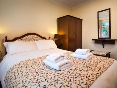 A bedroom with a bed and folded towels on a patterned bedspread a wooden wardrobe and a wall mirror at Nutwood in Lakeside