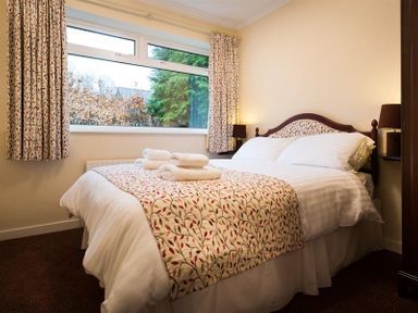 A bedroom with a double bed white bed linens patterned bedspread and curtains large window at Nutwood Lakeside